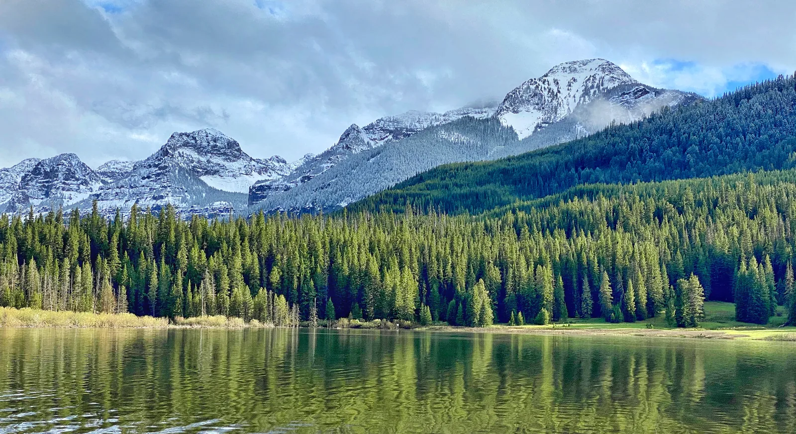 Alpine lake reflecting pine forest and snow-covered peaks in the Montana mountains